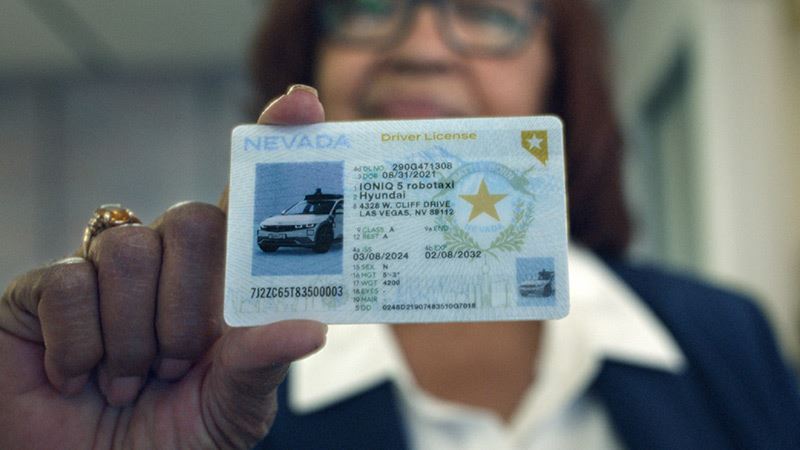 Rijexaminator Kandice Jones toont het kersverse (fictieve) rijbewijs van de zelfrijdende Hyundai IONIQ 5-robotaxi.