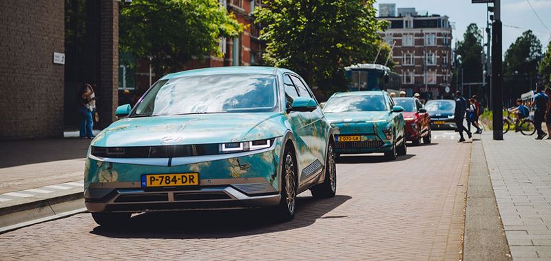 Een IONIQ 5 met daarachter een KONA Electric. Beide elektrische Hyundai’s zijn gehuld in de kleuren van het schilderij Amandelbloesem van Vincent van Gogh.